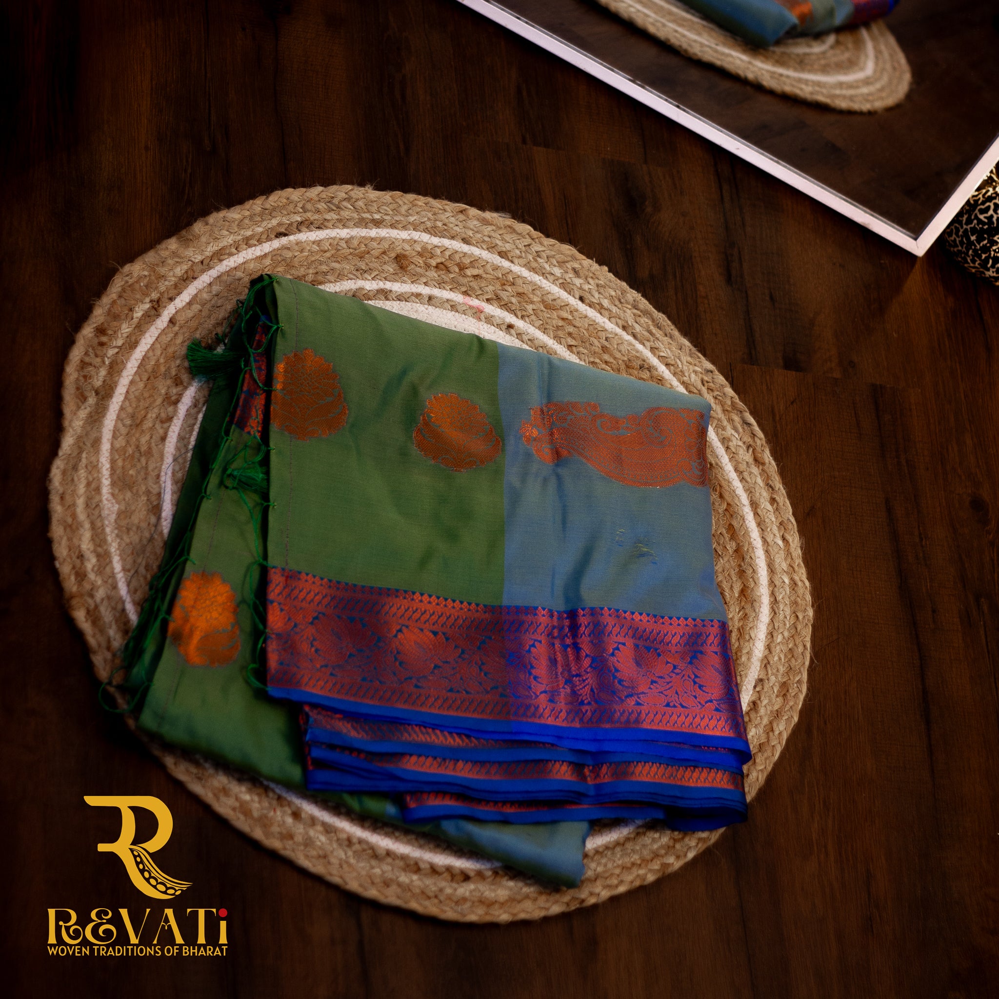 Moss green and sky blue soft silk saree adorned with copper-toned mango and floral motifs, finished with elegant violet-pink zari woven borders.