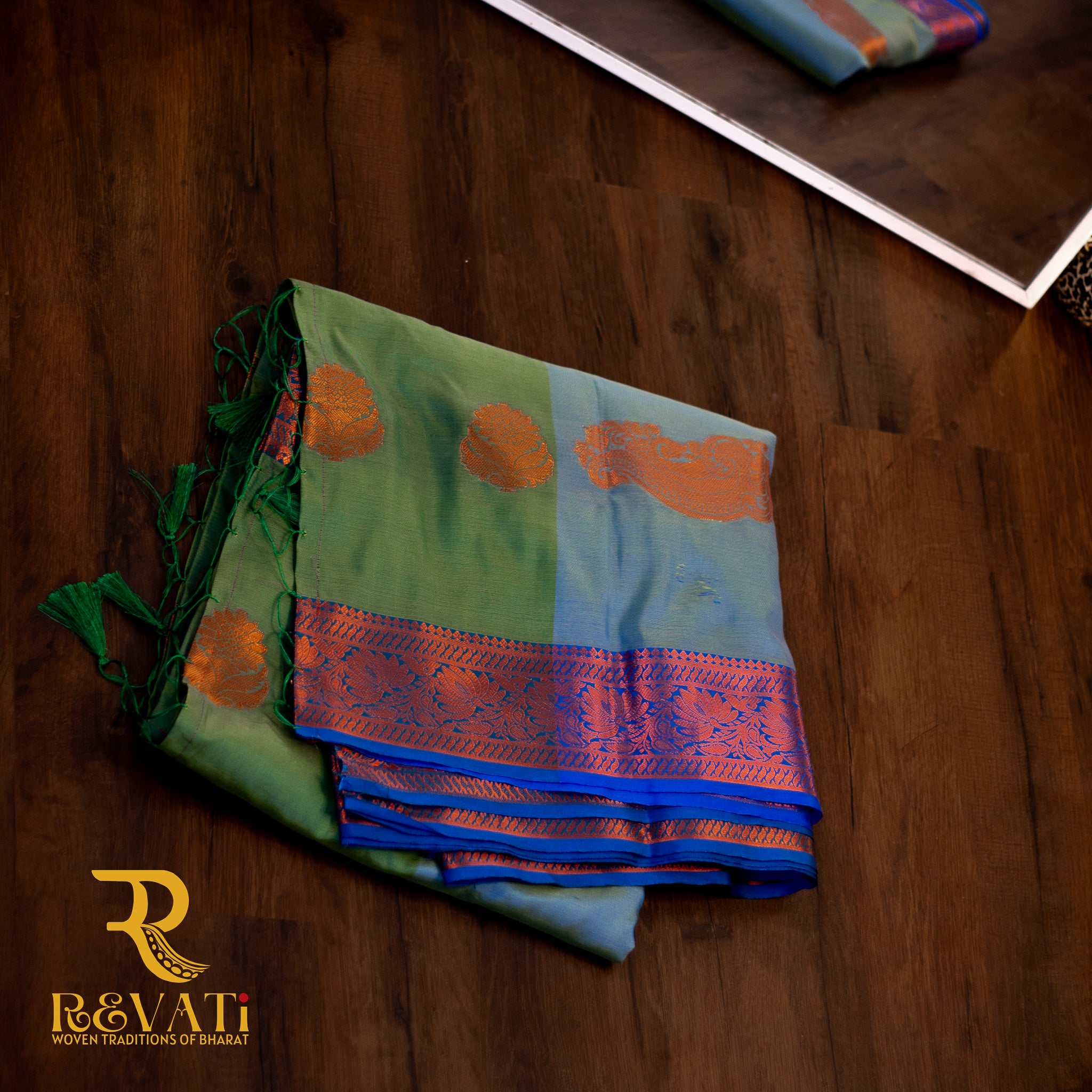 Moss green and sky blue soft silk saree adorned with copper-toned mango and floral motifs, finished with elegant violet-pink zari woven borders.