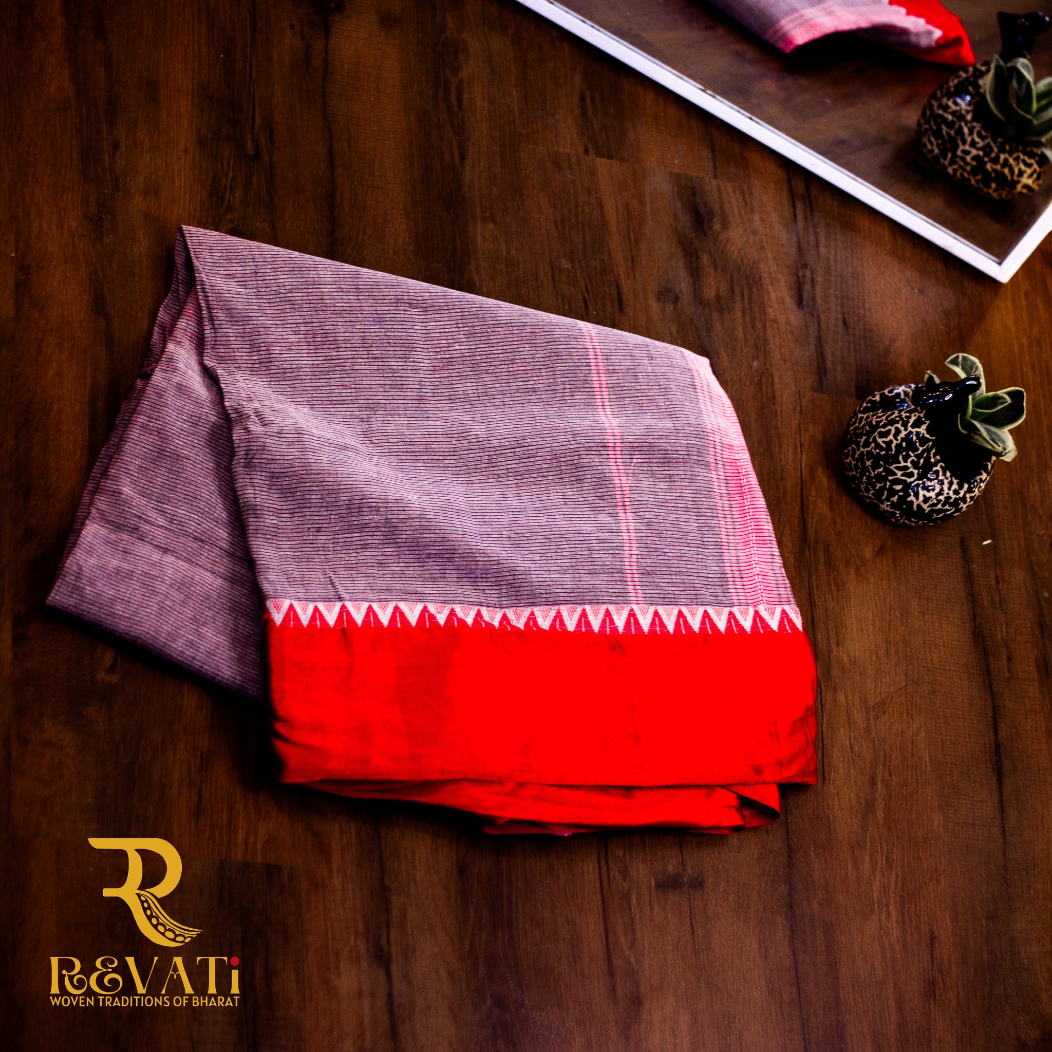 Charcoal grey handwoven cotton saree featuring a subtle linear self-weave, striking red zigzag borders, and effortless everyday elegance.